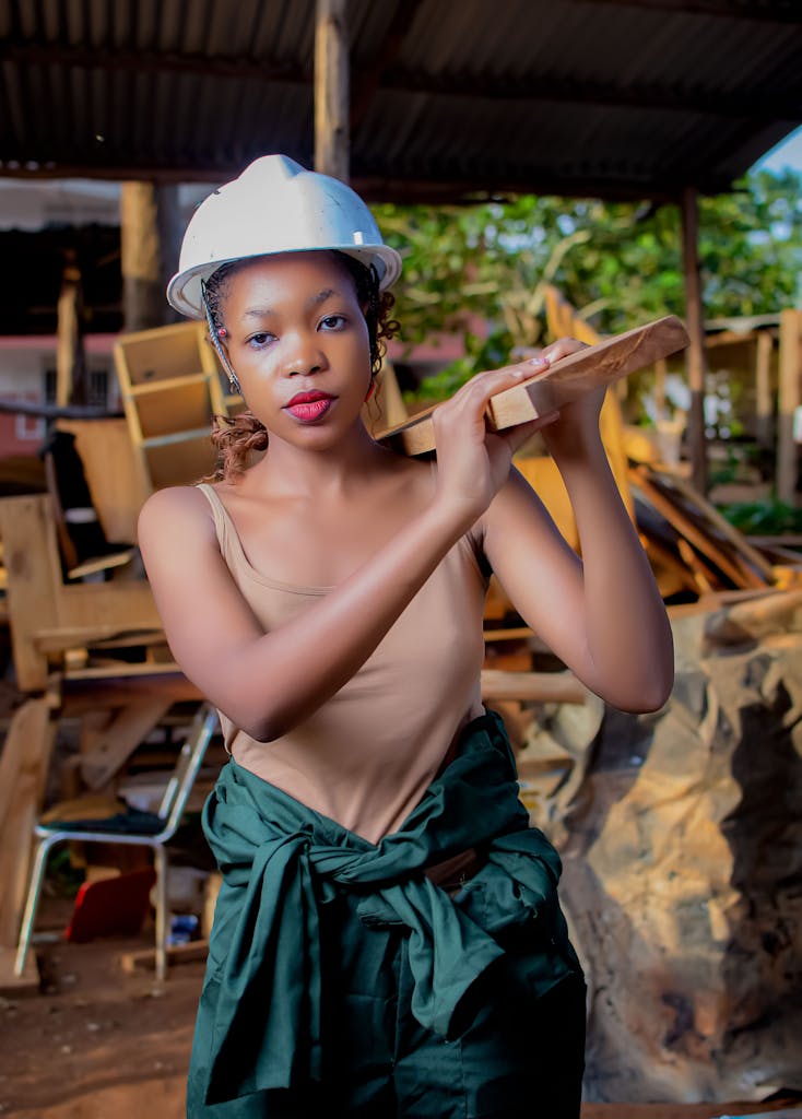 Confident female construction worker poses with wood plank at outdoor site.