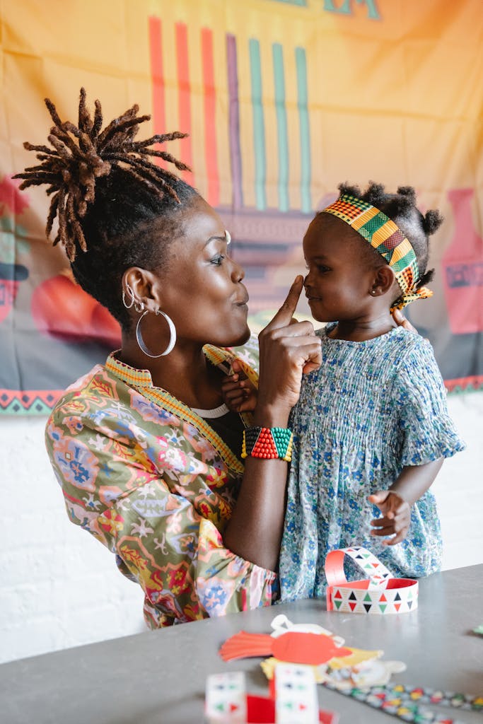Mother and daughter share a playful moment in colorful traditional clothing indoors.